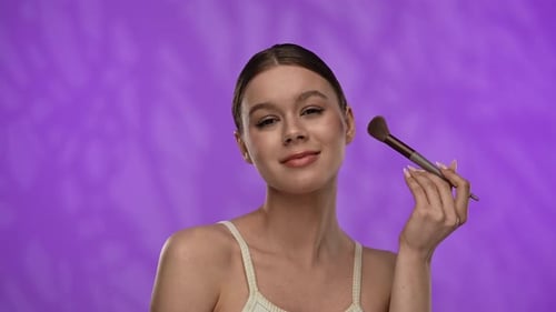 Young Woman with Makeup Posing at Camera in Studio Playfully Smiling Touching Applying Blushes with