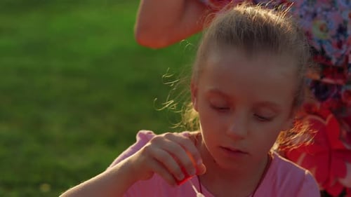 Cute girl blowing soap bubbles in slow motion with mother at sunset in city park
