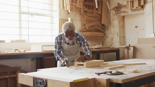 African american male carpenter hammering nails into the wood at a carpentry shop