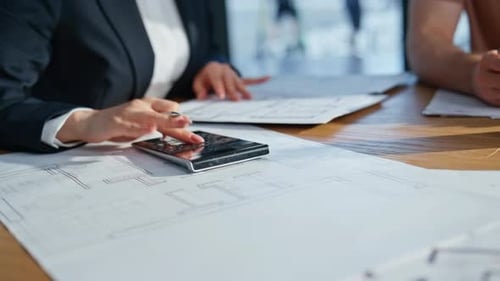 Geschäftsfrau drückt bei der Arbeit auf Taschenrechner und analysiert Dokumente in Nahaufnahme