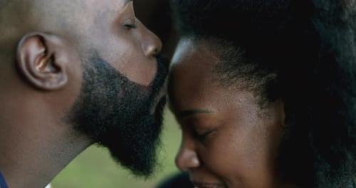Affectionate Man Kissing Woman in Green Outdoor Setting