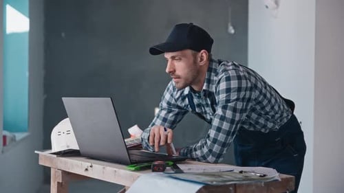 A Man is Standing at a Desk with a Laptop Computer