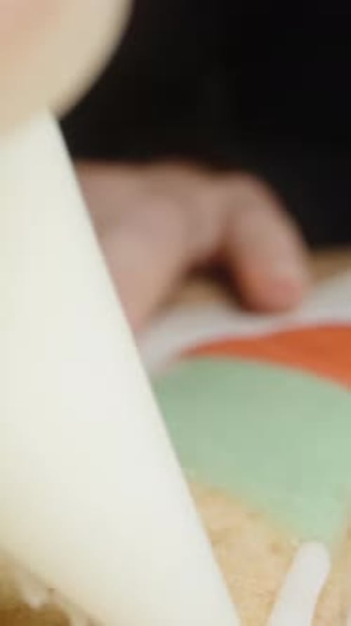 Vertical video. The camera moves back, capturing a macro shot of icing flowing from the pastry bag o