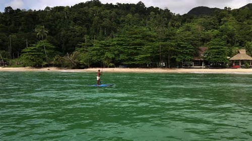 low angel Aerial drone tracking shot of Asian man exercising on a sup paddle board in turquoise trop