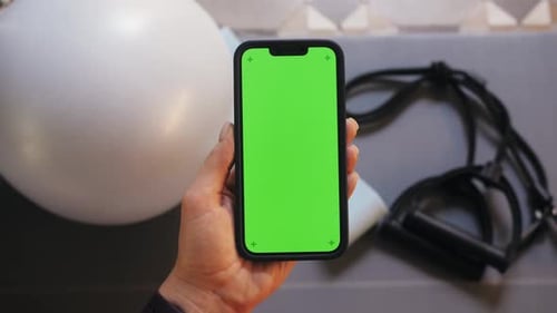 Woman Holding Green Screen Smartphone In the Background Fitness Mat Jumping Rope and Equipment