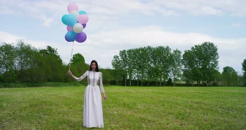 Woman Holding Colorful Balloons in Green Field