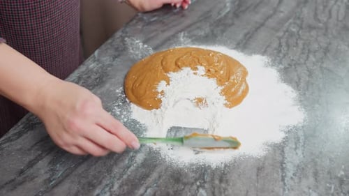 Aerial View of Woman Covering Brown Dough with Flour Using Green Spatula