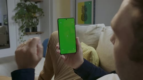 Digital Interaction: Person Touches Green Screen Smartphone on Sofa