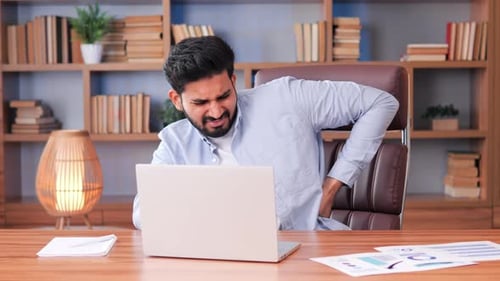 Exhausted Busy Indian Businessman Works on His Computer Having Back Pain