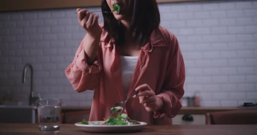 Young Adult Woman Eating Healthy Salad in Kitchen