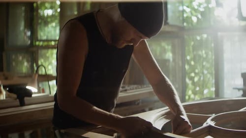 Bearded Carpenter Works on Round Wooden Frame in Carpentry Shop