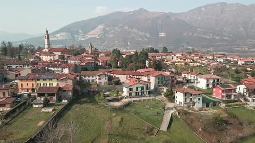 Rural Village With Residential Houses And Church Tower Set Amidst Green Meadows And Beautiful Mounta