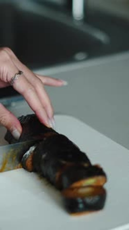 Female Hands Slicing Grilled Eggplantresting on White Cutting Board Near Kitchen Counter
