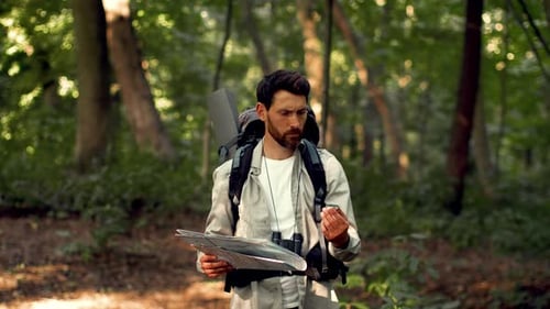 Homem com pele clara explorando a floresta enquanto segura um mapa e binóculos durante a aventura diurna