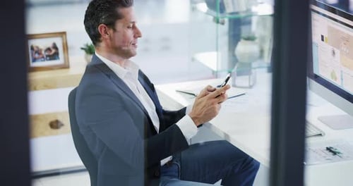 4k video footage of a handsome young businessman sitting alone in his office and using his cellphone