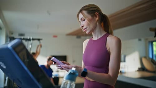 Woman Walking on Treadmill Uses Smartphone at Gym