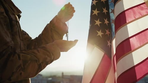 Soldier Holds Dog Tags Beside American Flag at Sunrise