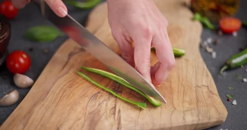 Woman Cutting Green Chili Pepper on a Wooden Cutting Board at Domestic Kitchen