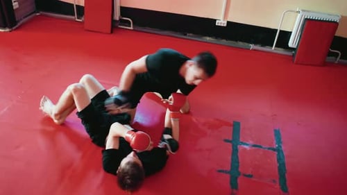Un luchador inmoviliza a su oponente en una alfombra roja durante una sesión de combate de artes marciales