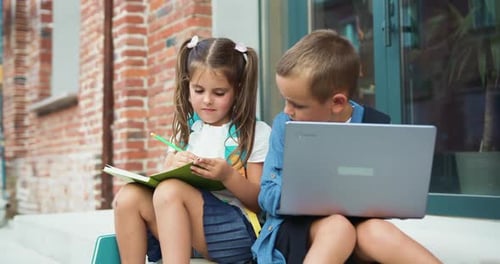Two school children pupils girl and boy classmates friends sitting on stairs street outdoors