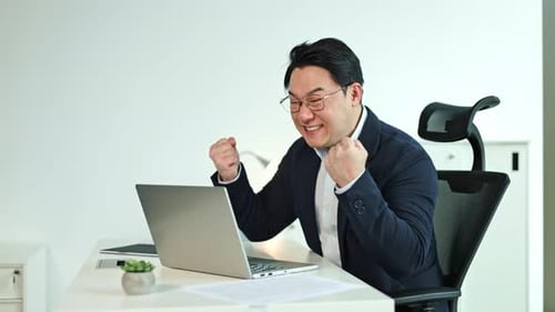Excited Businessman Celebrates Success While Working on Laptop in Office