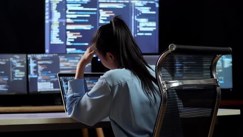 Rückansicht einer asiatischen Programmiererin, die beim Schreiben von Code mit einem Laptop Kopfschmerzen hat