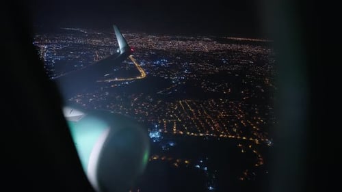 Airplane Wing Flying Over Illuminated City at Night