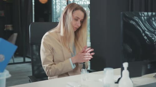 Blonde Attractive Woman Applying Sanitizer Spray Rubbing Her Hands at Working Desk in the Office