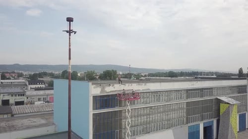 Aerial rotation around industrial workers with crane lift next to metal warehouse doing work on roof