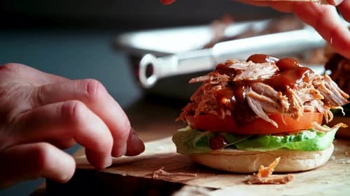 Chef Assembling a Gourmet Pulled Pork Burger with Barbecue Sauce