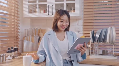 Woman Using Tablet and Drinking Coffee in Kitchen