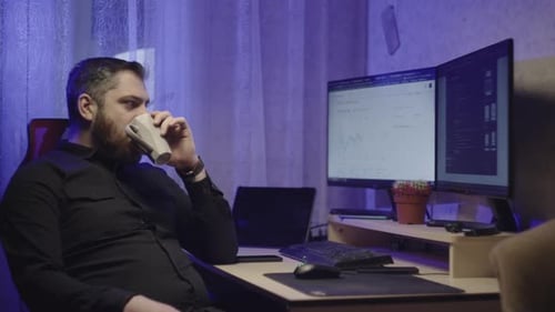 A Businessman Works at a Computer at Home and Drinks Coffee From a Cup on Break