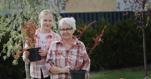 Portrait of an Elderly Woman with Her Granddaughter Holding Potted Plants for Planting in the Garden