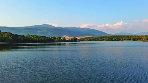 See mit klarem Wasser und Steinufer im Fichtenwald mit Tannen vor einem Tageshimmel