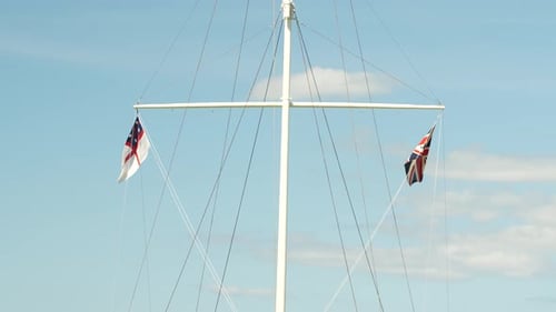 UK Flags Fluttering on White Flagpole Against Blue Sky