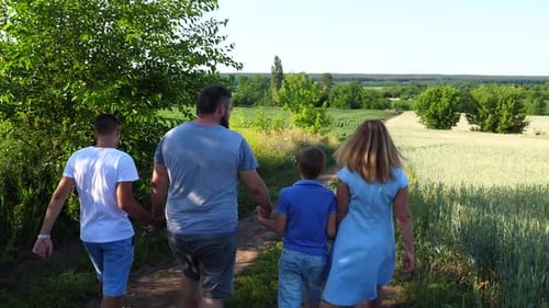 Young Parents with Two Sons Hold Hands of Each Other Walking Along Path Near Green Meadows Mommy and