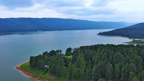 Lake with Clear Water and Stone Shore in Spruce Forest with Fir Trees Against a Daytime Sky