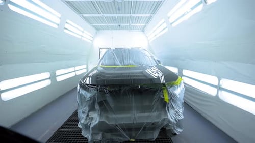 Freshly Painted Black Car Inside Professional Automotive Paint Booth with Bright Lights