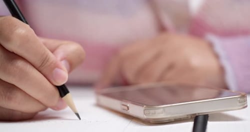 Frau schreibt persönliche Einnahmen und Ausgaben von ihrem Telefon zur Finanzanalyse in ein Notizbuch