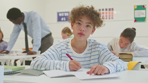 Student Writing in Classroom Looks Up and Smiles
