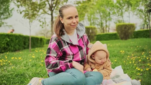 A Mother and Her Baby Enjoy a Beautiful Spring Day in the Park They are Sitting on a Blanket