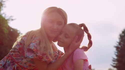 Smiling Woman Hugging Adorable Girl in City Park at Sunset. Happy Mother