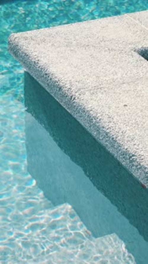 Clear blue water in the pool. Steps into the pool. The edge of the pool is finished with a gray curb