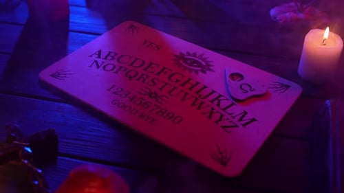 Close Up Video of a Wooden Ouija Board on a Table Surrounded By Candles Candlesticks and Other