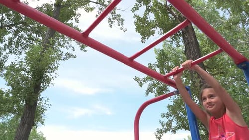 Girl Hanging From Monkey Bars In Park