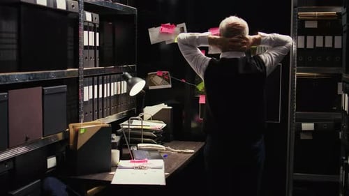 Man Leans on Desk Thinking in Small Dark Office