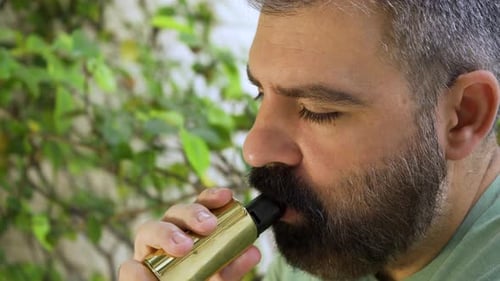 Close up of bearded men inhaling e-cigarette device in daylight 01.