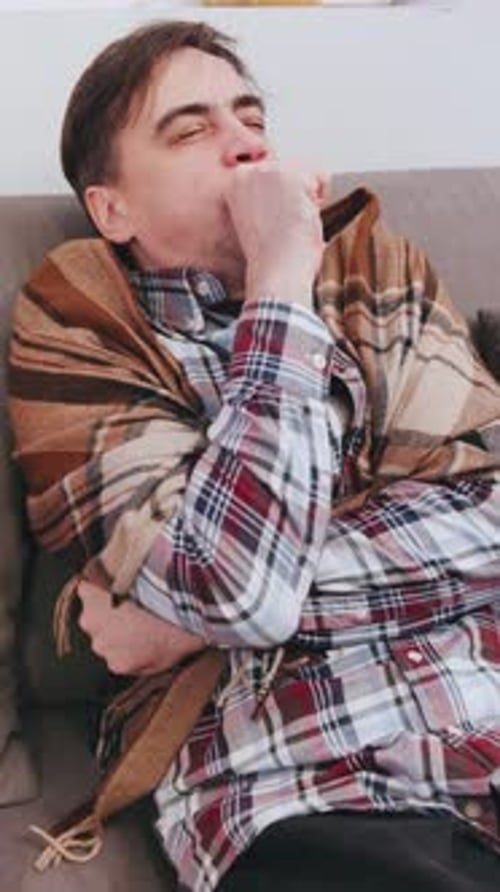 Vertical Video Senior Man Sitting on Couch Wrapped in a Blanket Shivering and Coughing in a Cozy