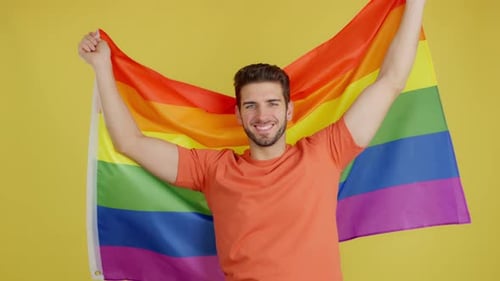 Smiling Person Waving Rainbow Pride Flag on Yellow
