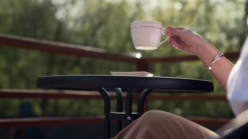 Female Hand Takes Porcelain Coffee Cup on Cozy Terrace in Peaceful Morning Light